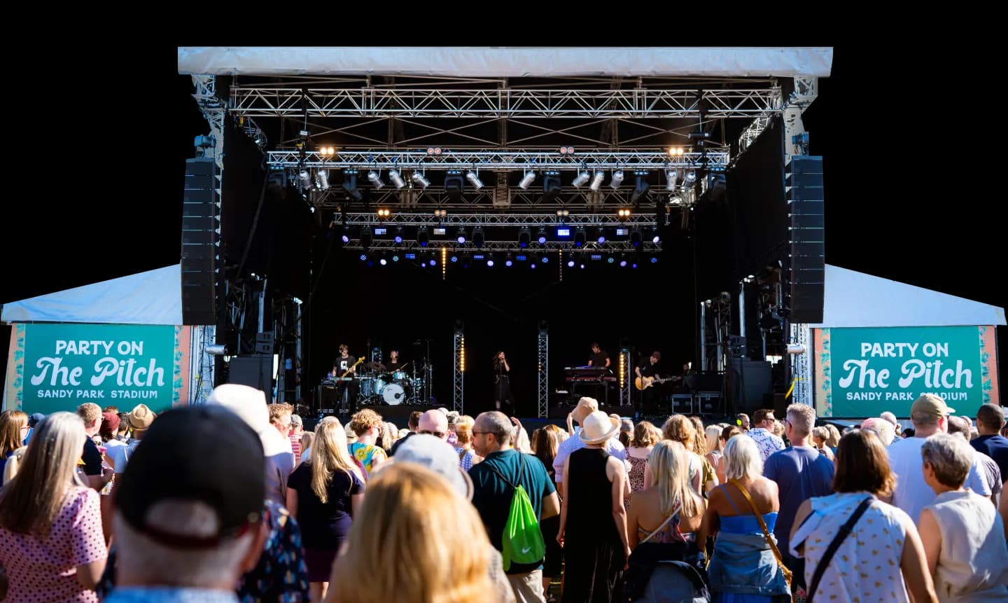 a crowd standing in front of a stage at party on the pitch